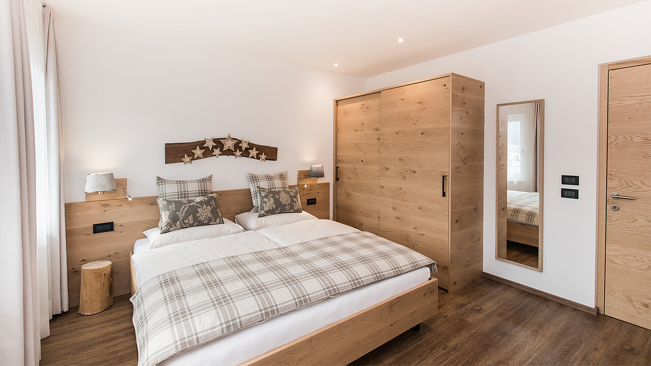 Bett und Kleiderschrank des Doppelzimmers des Apartments Seceda in St. Ulrich